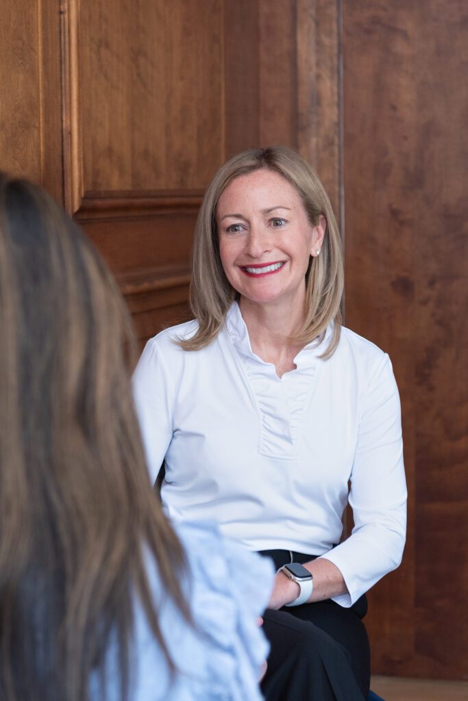 A female college consultant wearing a white top and black pants sitting and talking to her client.