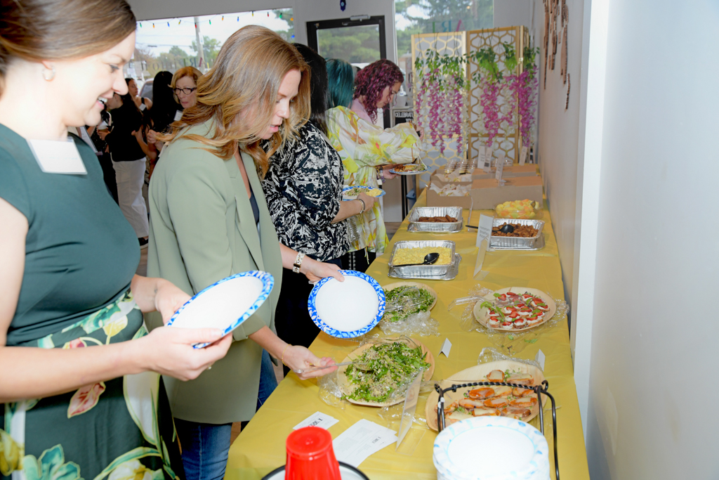 The attendees of the Canvas & Connections: Celebrating Women Business Owners event are getting brunch at the table with salads, crostinis, wraps, fruits, and cupcakes.