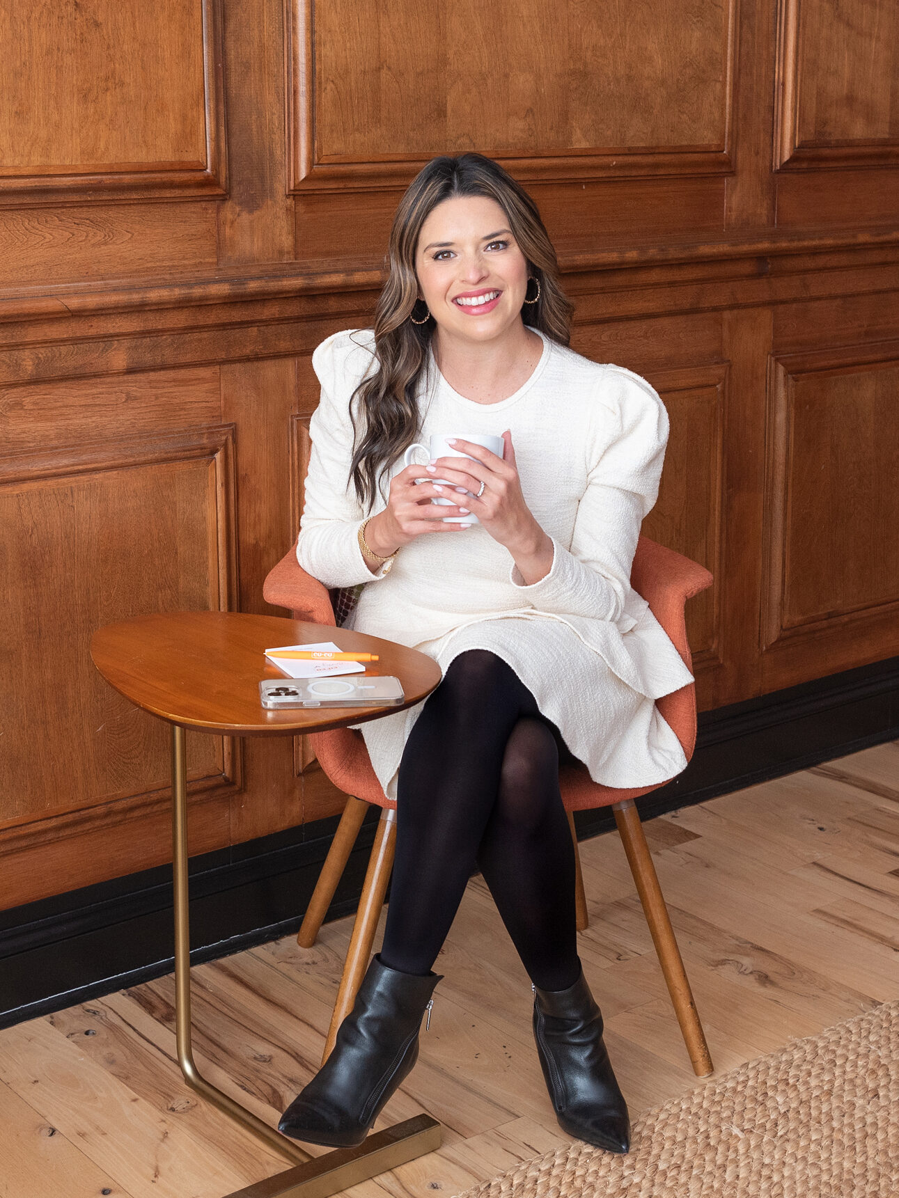 A Latino women in a white dress and black legging holding a cup of coffee at her favorite coffee shop.