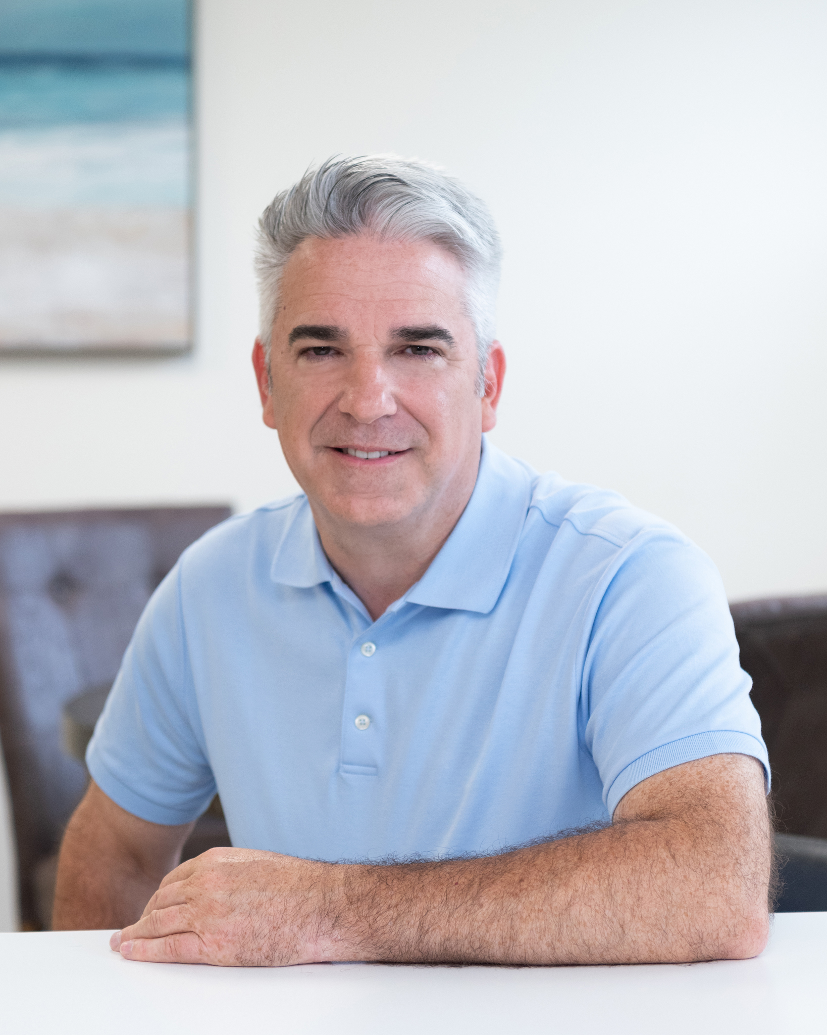 A male business coach wearing a light blue collar shirt sitting in an office space.