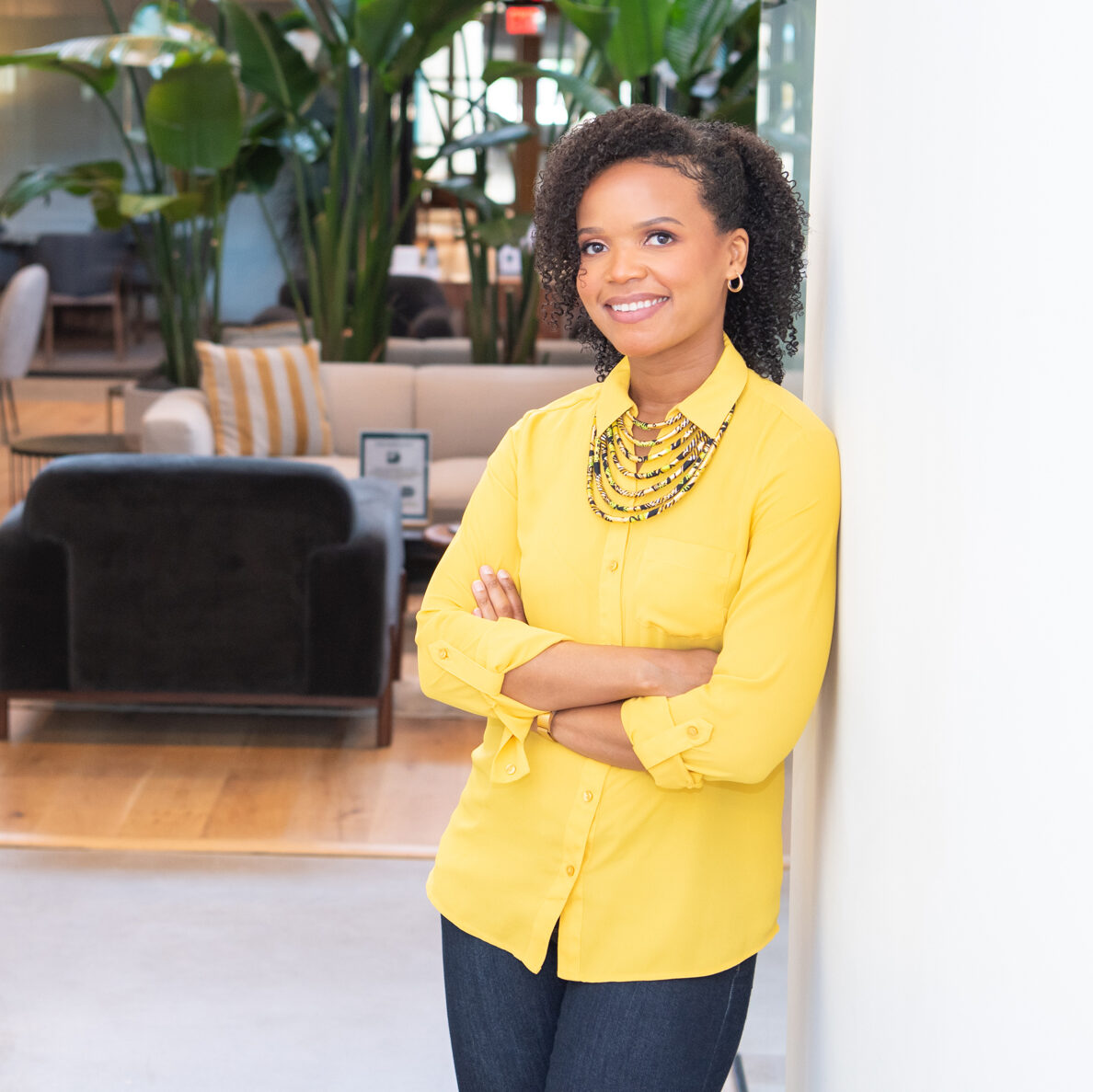 An African American female business attorney in a yellow shirt posing with her arm crossed for her branding photoshoot.