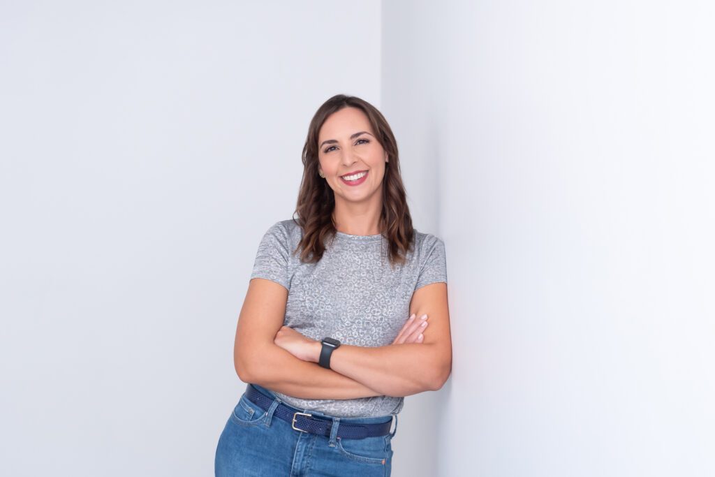 A female website designer with a silver t-shirt and jeans leaning against the wall and posing for her personal branding photo session.
