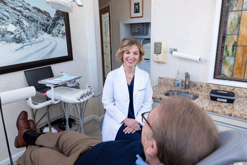 A female dentist smiling and talking to her patient in the dental exam room.