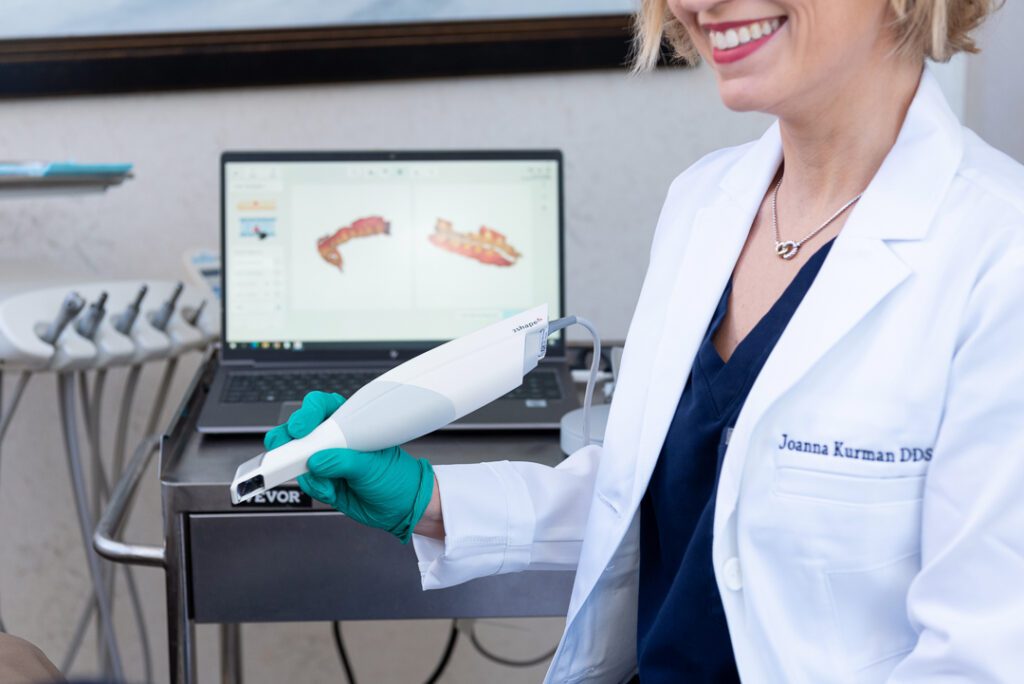 A female dentist smiling and holding a device for scanning teeth.