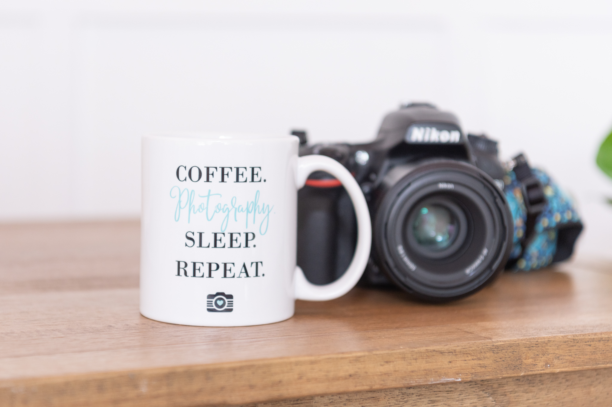 A mug with the words "Coffee. Photography. Sleep. Repeat." and a Nikon camera behind it.