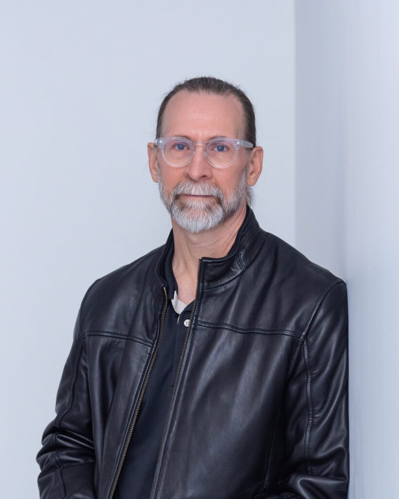 A male product and jewelry photographer wearing a leather jacket and posing for his headshot.