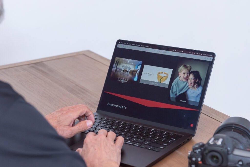 A male product and jewelry photographer showing his website at his office with his camera on the side of the laptop.