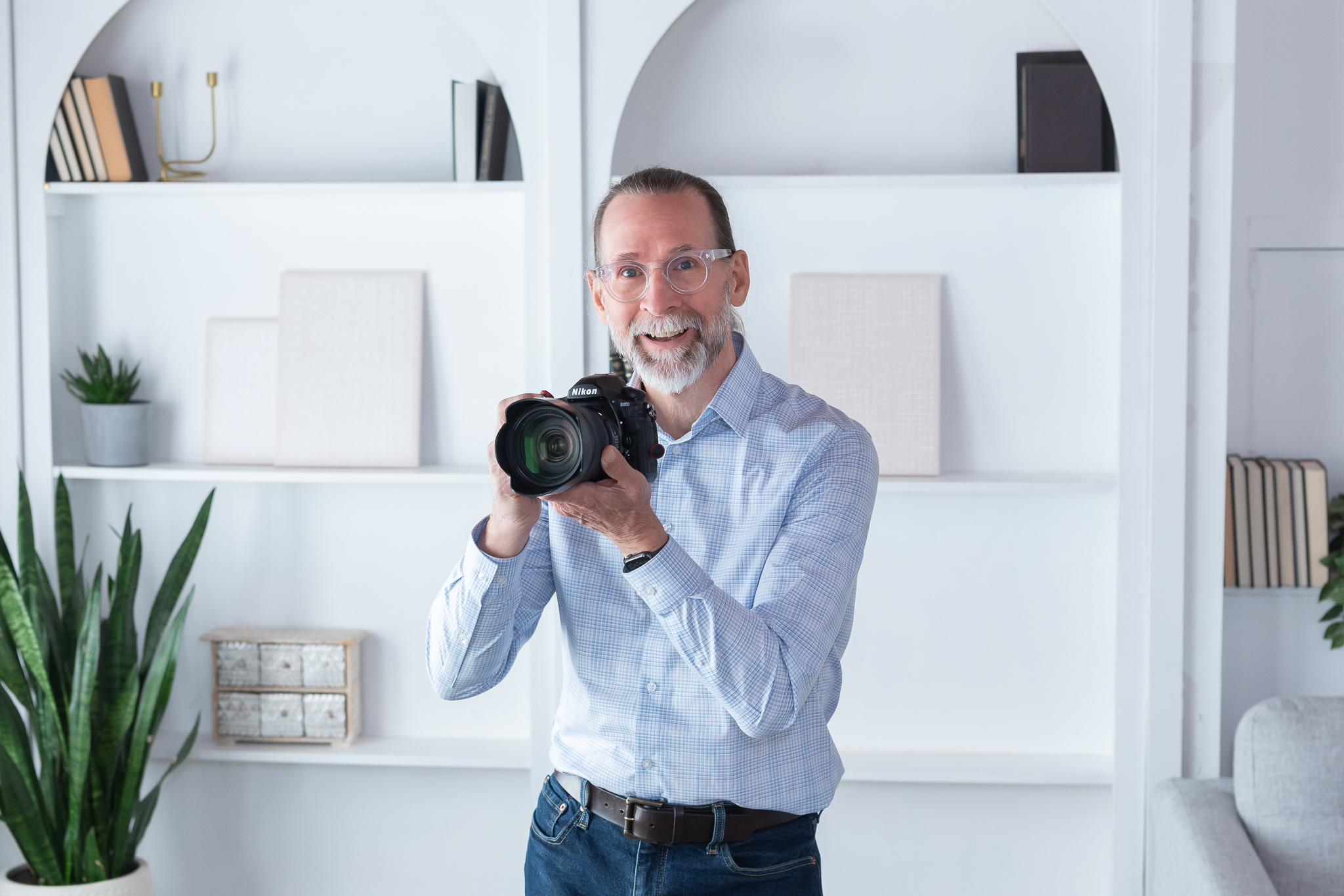 A male product and jewelry photographer holding his camera and standing in front shelf at his branding photo session.