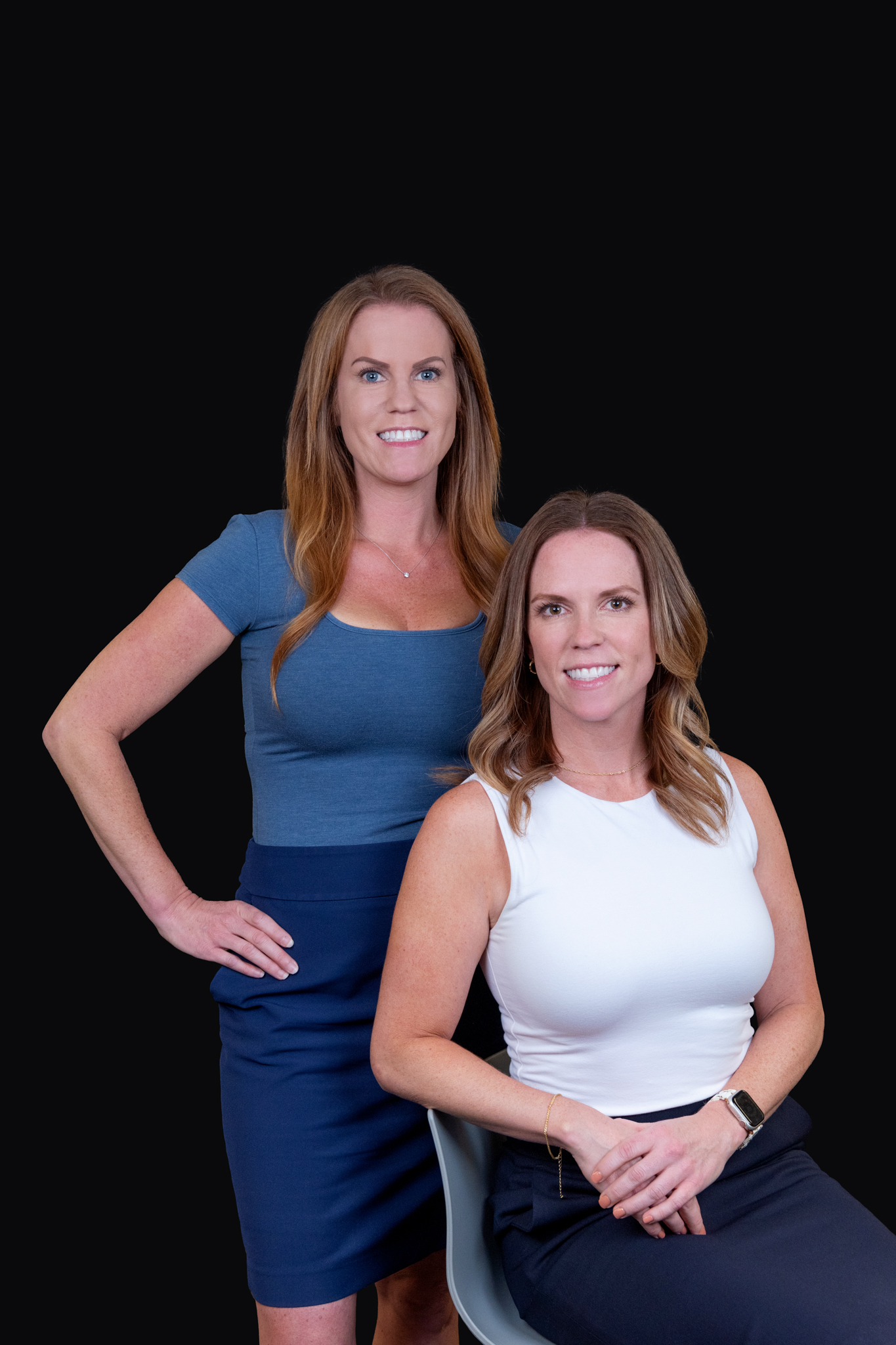 CEO & COO of Hanson & Ryan Inc. Two female business owners posing for their headshots for their website. One with white top and sitting, the other with a blue top and standing.