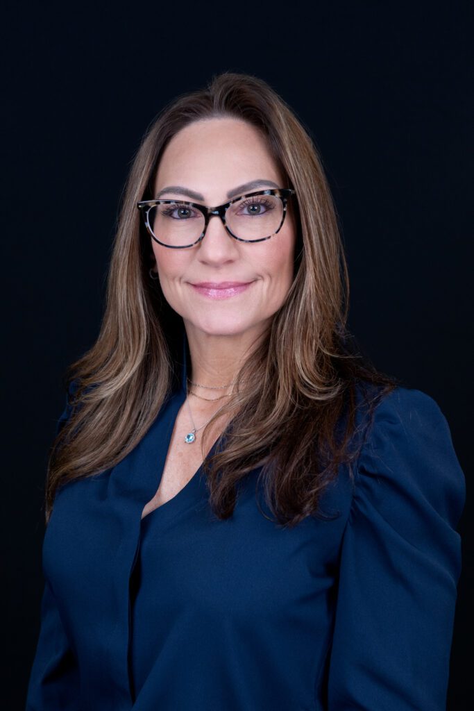 A female insurance agent with a navy blue top is posing for her headshot with a black backdrop.
