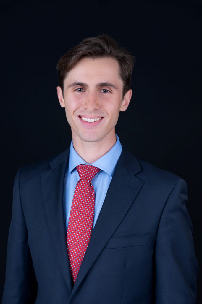 A male insurance agent with a maroon colored tie is posing for his headshot with a black backdrop.