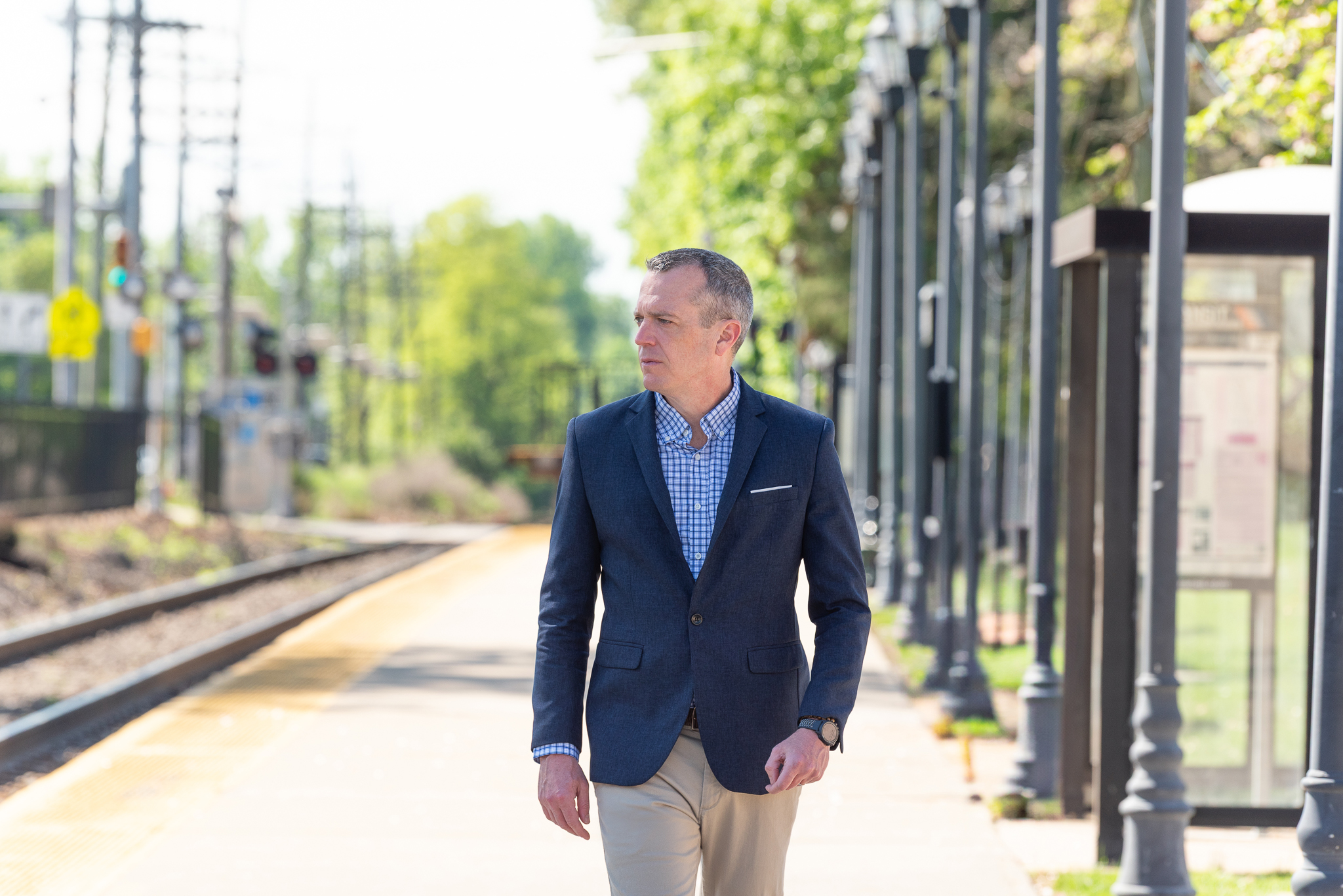 A male international keynote speaker's branding photo of him in a suit walking on a train station platform.