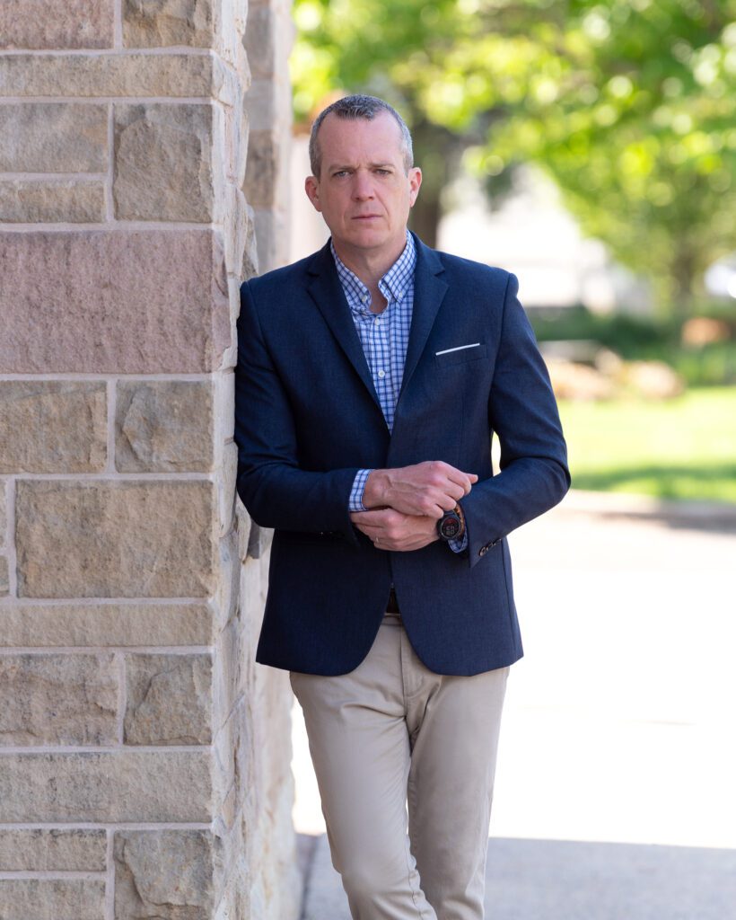 A male international keynote speaker in a suit is posing with his hands on his sleeve for his branding photoshoot.