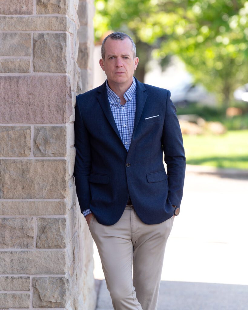 A male international keynote speaker in a suit is posing for his headshots.