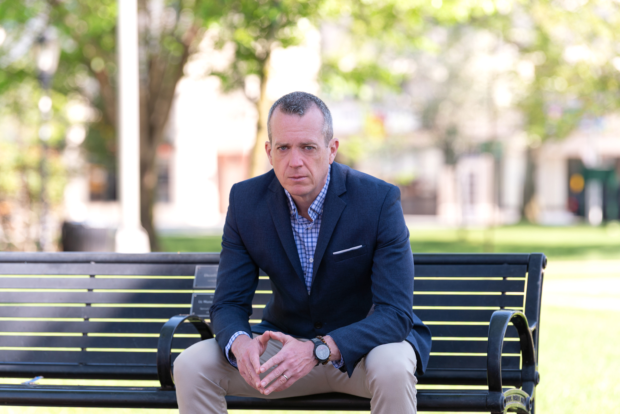 A male international keynote speaker's branding photo of him in a suit sitting on a park bench.