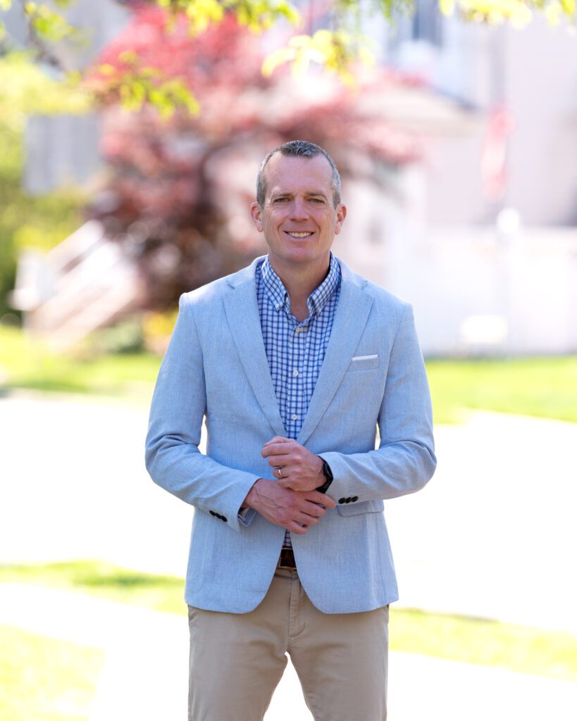A male international keynote speaker in a light blue suit is posing with his hands on his sleeve for his branding photoshoot.