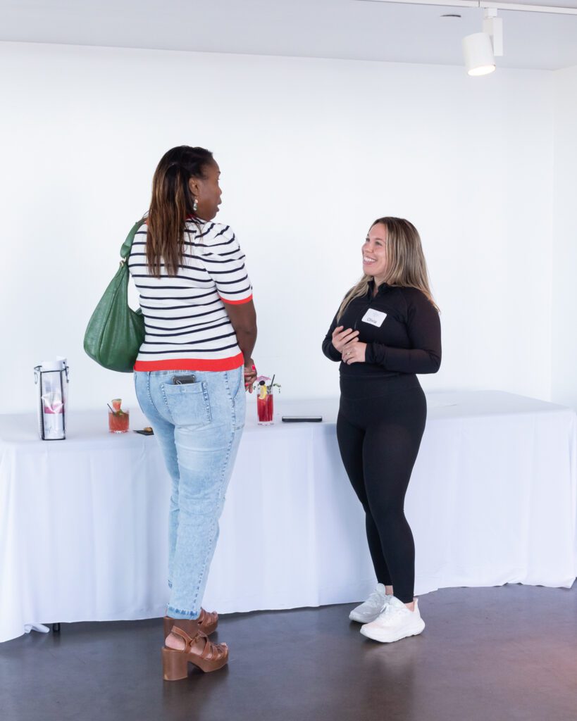Two female attendees conversing with each other while enjoying mocktails and food at the Your Strategy Reset event in the Wave Resort.