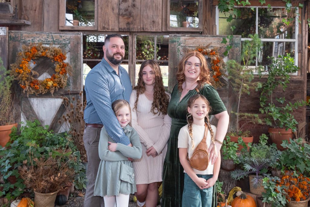 A family of 5 posing in front of a fall theme background for their family portrait session.
