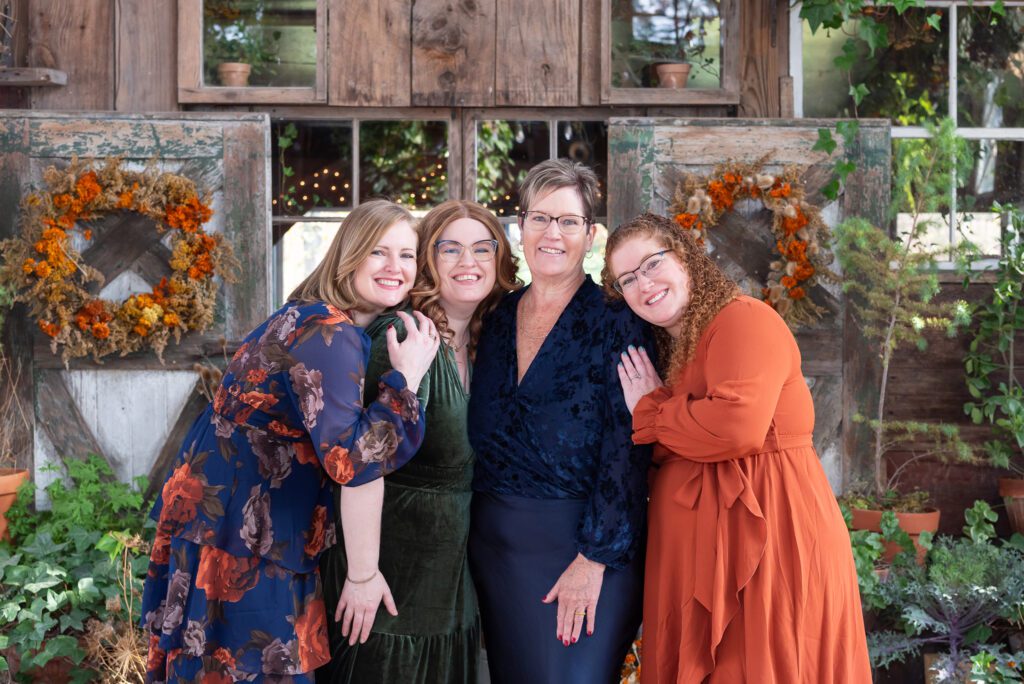A mom and her 3 adult daughters hugging each other in front of a fall theme background for their family portrait session.