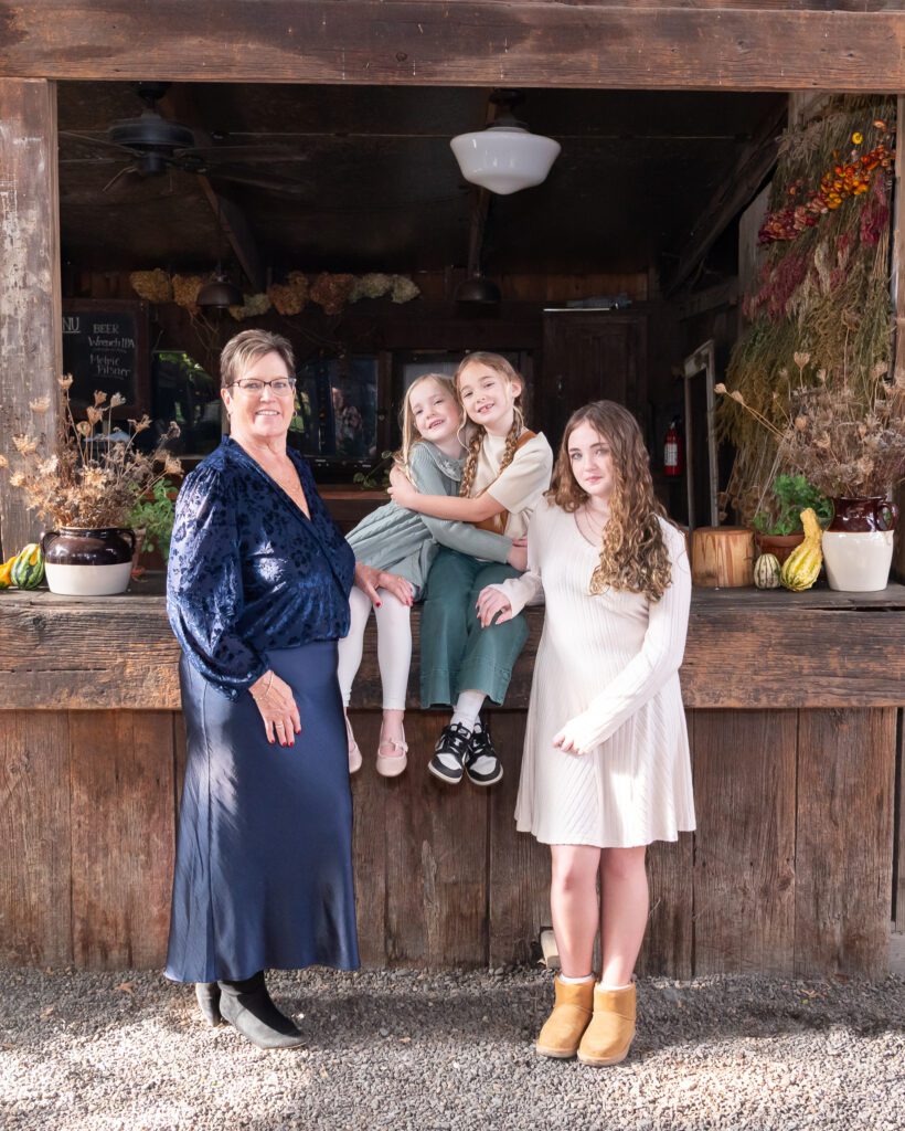 A grandmother with her 3 granddaughters posing inside a barn for their family photo session.