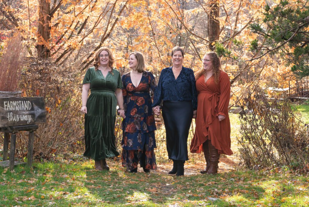 A mom and her 3 adult daughters holding hands and laughing during their family portrait session.