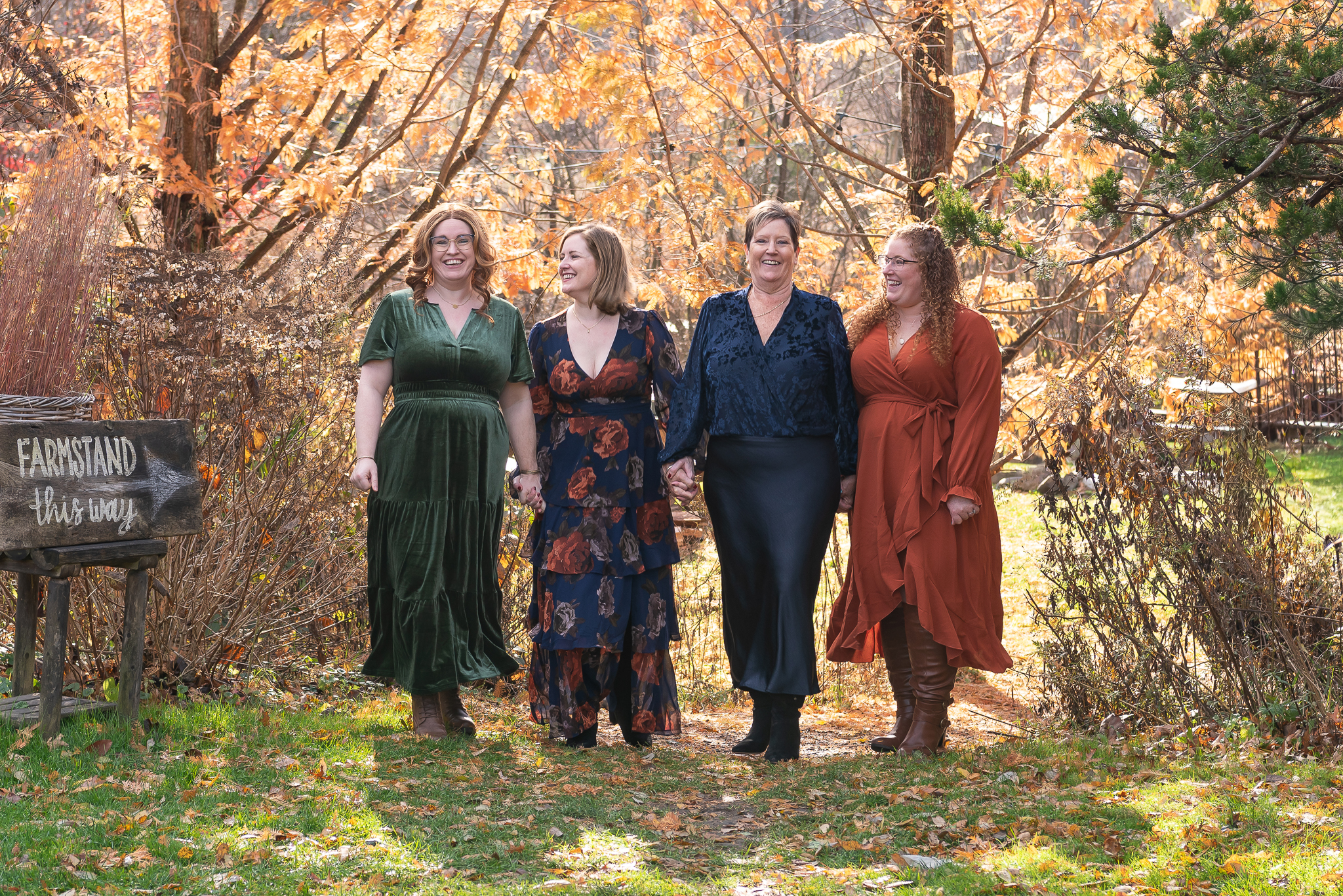 A mom and her 3 adult daughters holding hands and laughing during their family portrait session.