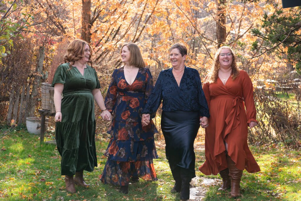 A mom and her 3 adult daughters holding hands and laughing during their family portrait session.
