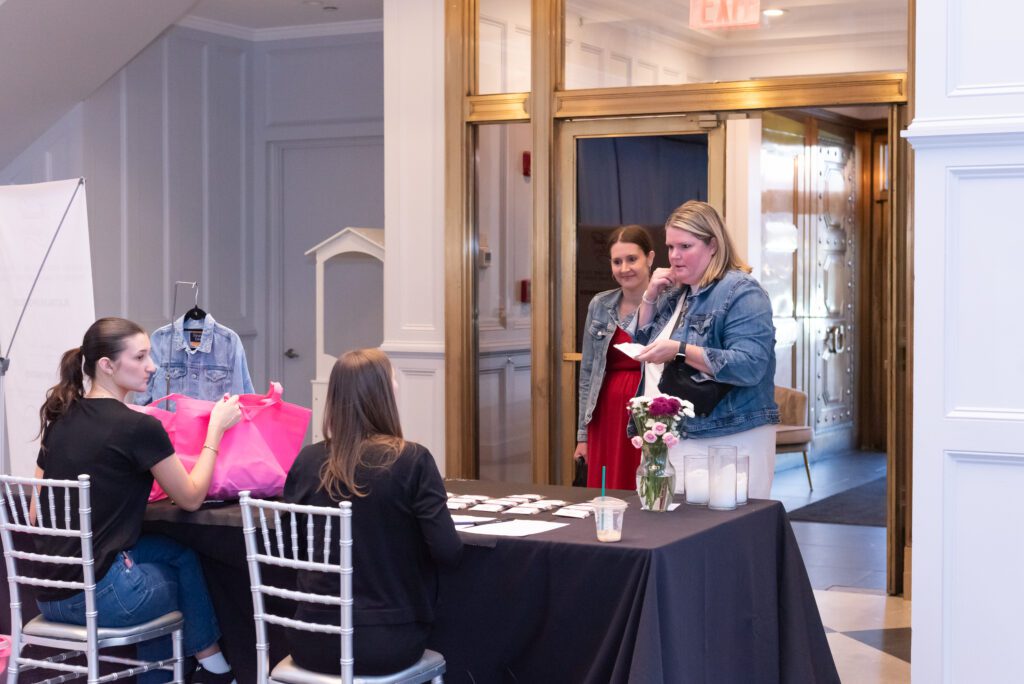Two women walking into and event at the check in table and were greeted by two volunteers.