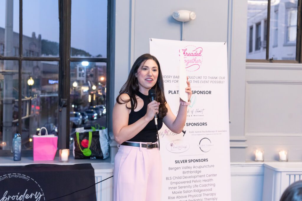 The female entrepreneur and owner of an embroidery company is holding a mic and giving her speech at her event.