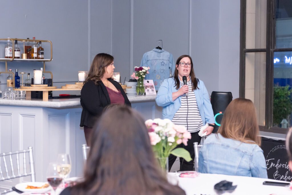 A woman is holding a mic while giving a speech with her sister standing next to her at an event.
