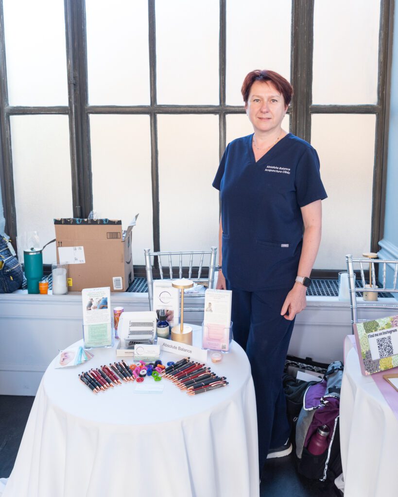 A female founder and owner of Absolute Balance Acupuncture posing and smiling at her vendor table.