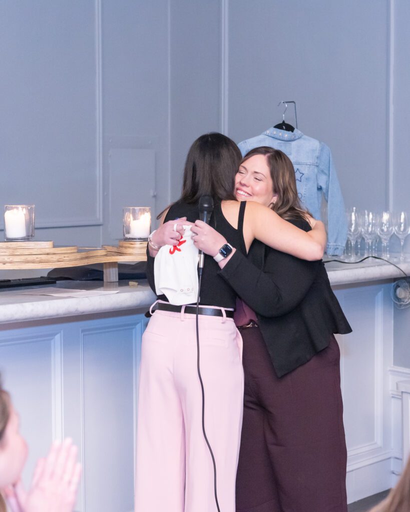 Two women are hugging at an event.