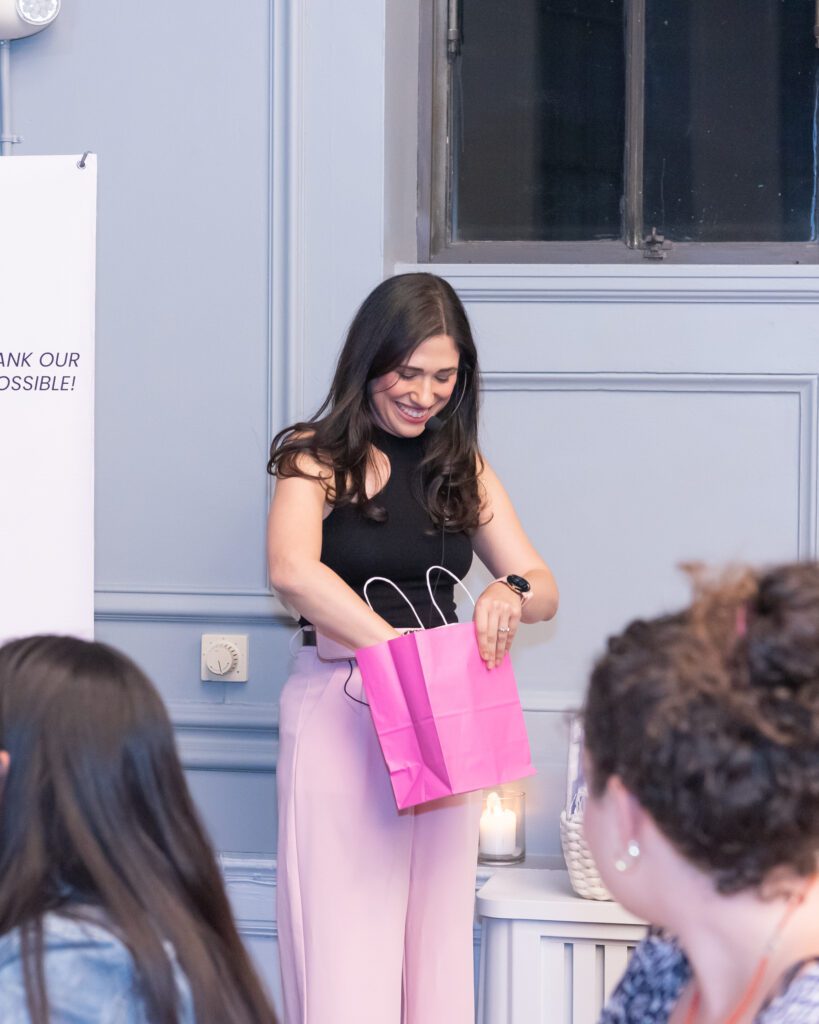 A woman is smiling and picking out a raffle number from a pink kraft bag at an event.