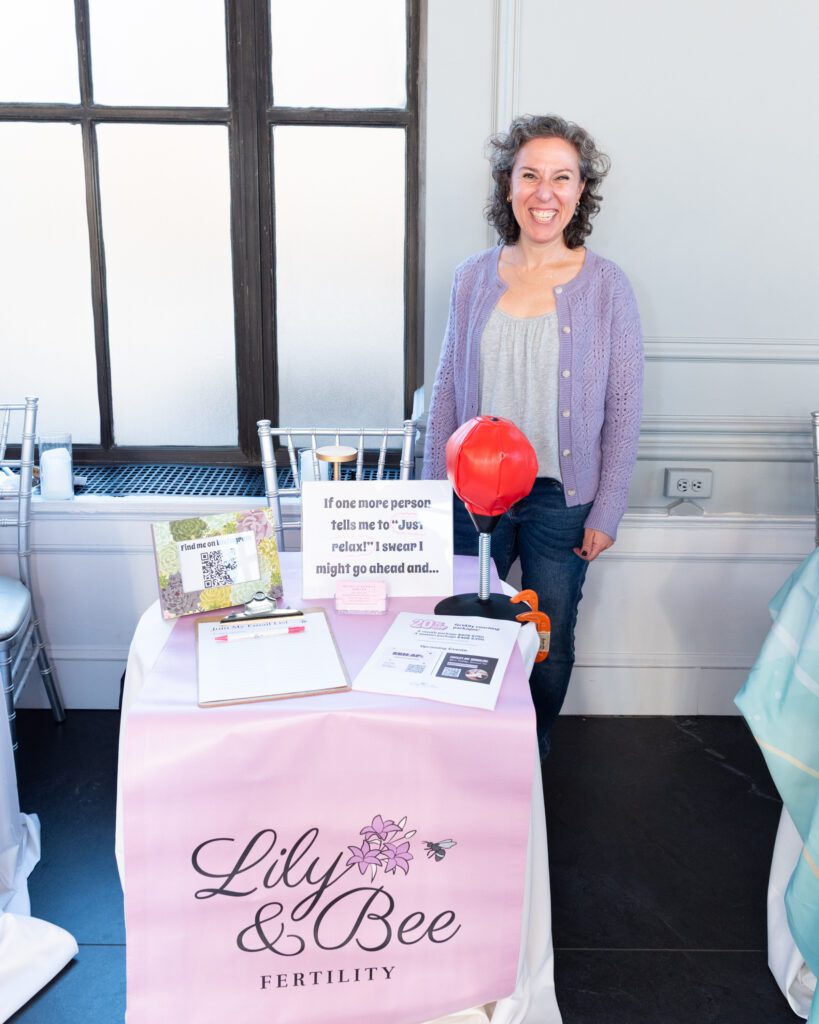 A female founder and owner of Lily & Bee Fertility posing and smiling at her vendor table.