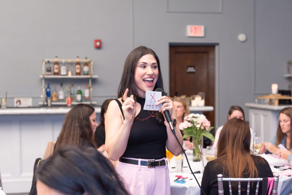 A woman is holding a mic and a swatch during her embroidery workshop.
