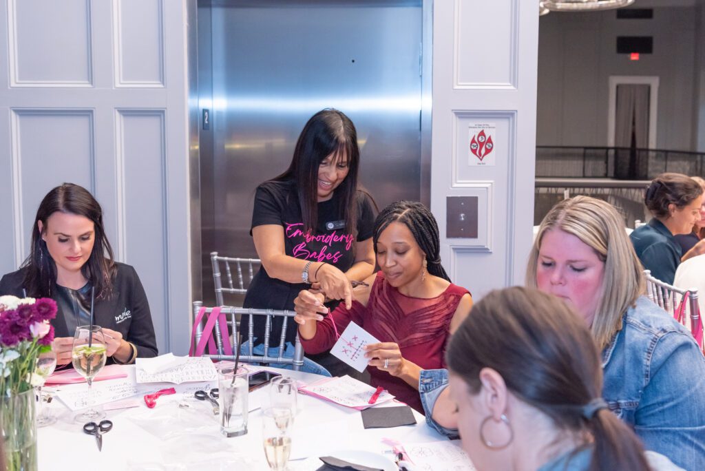A team member of the Embroidery Babes helping a woman with hand embroidery project.