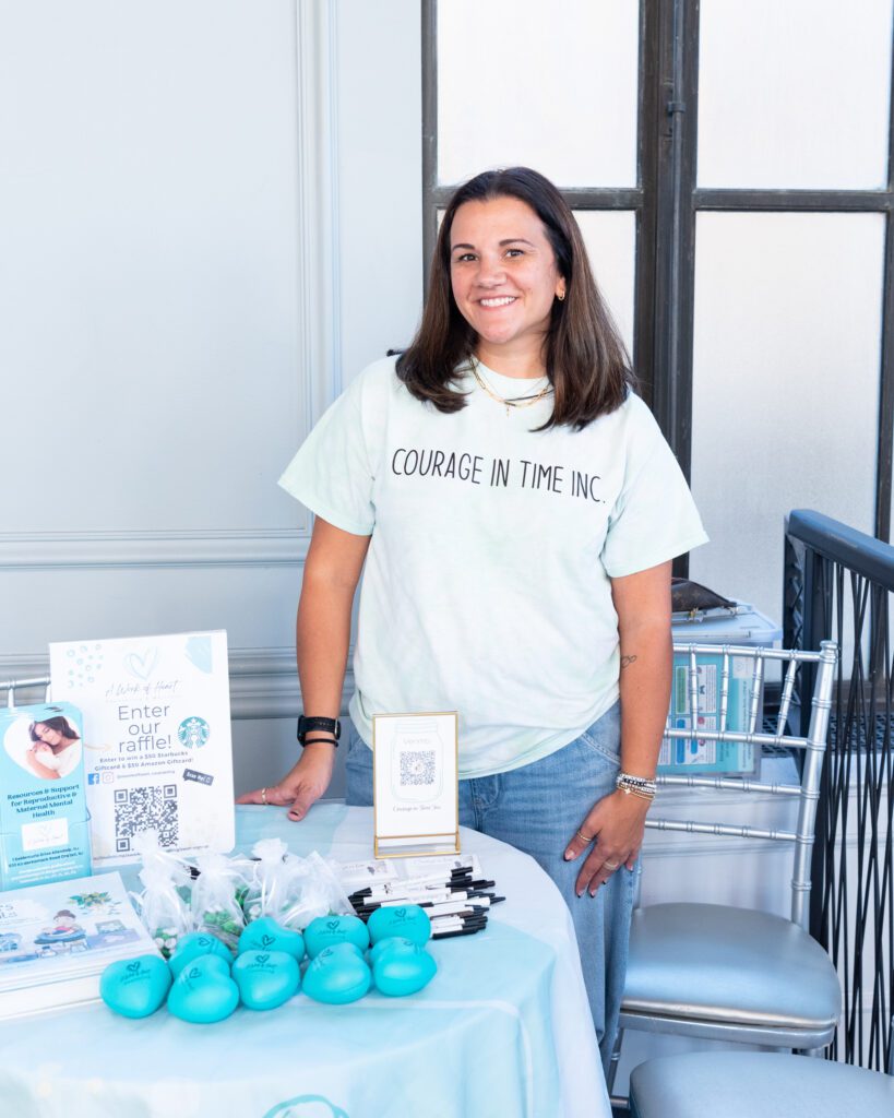 The female founder of Courage in Time posing and smiling at her vendor table.