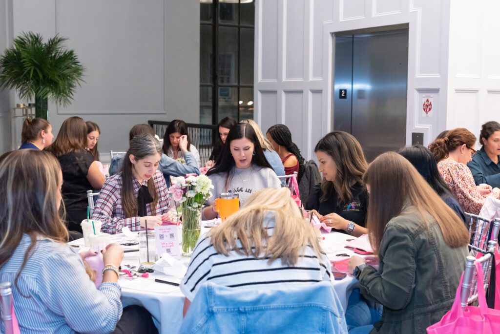 A group of women sitting at round tables, talking while hand embroidering at an embroidery workshop.