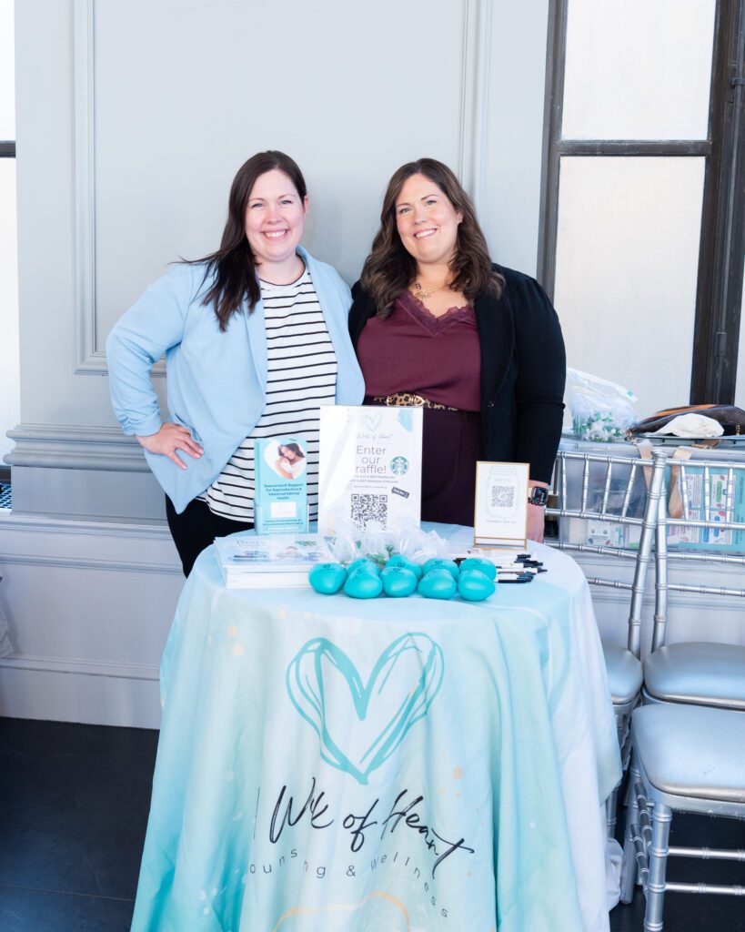 Two female owner and therapist from A Work of Heart Counseling in New Jersey posing and smiling at their vendor table.