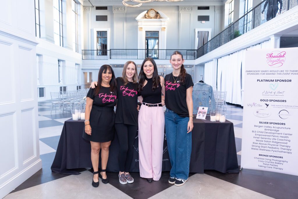 The female owner and host of the embroidery workshop posing and smiling for a picture with her team of volunteers at her event.