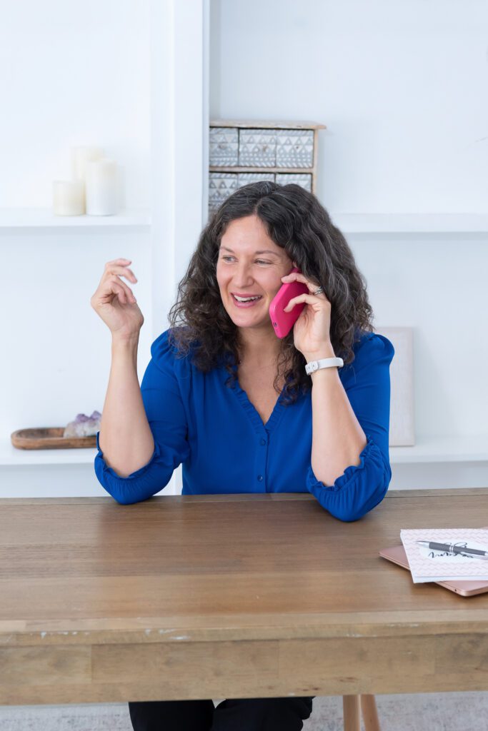 A female executive & leadership coach wearing a blue blouse and talking on her phone.
