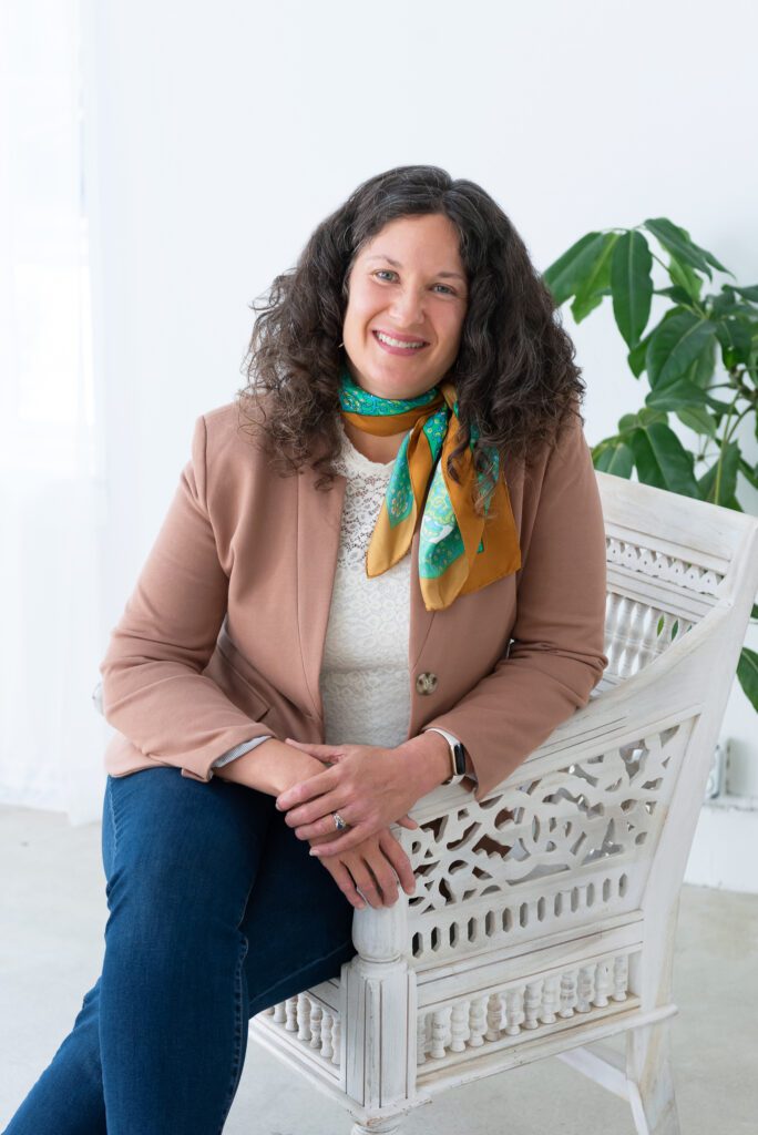 A female executive & leadership coach sitting and smiling with a beautiful scarf around her neck.
