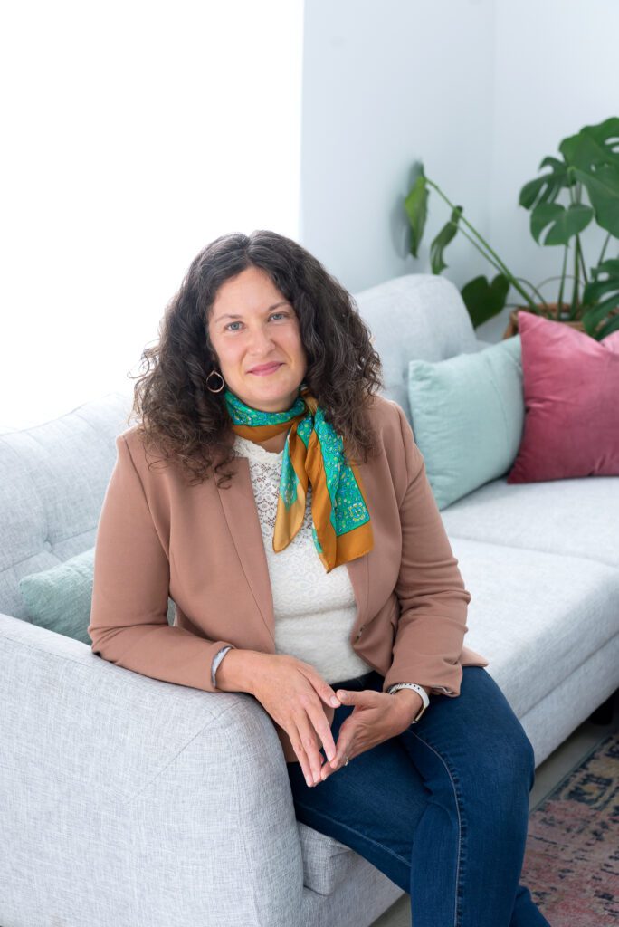 A female executive & leadership coach sitting and smiling with a beautiful scarf around her neck.