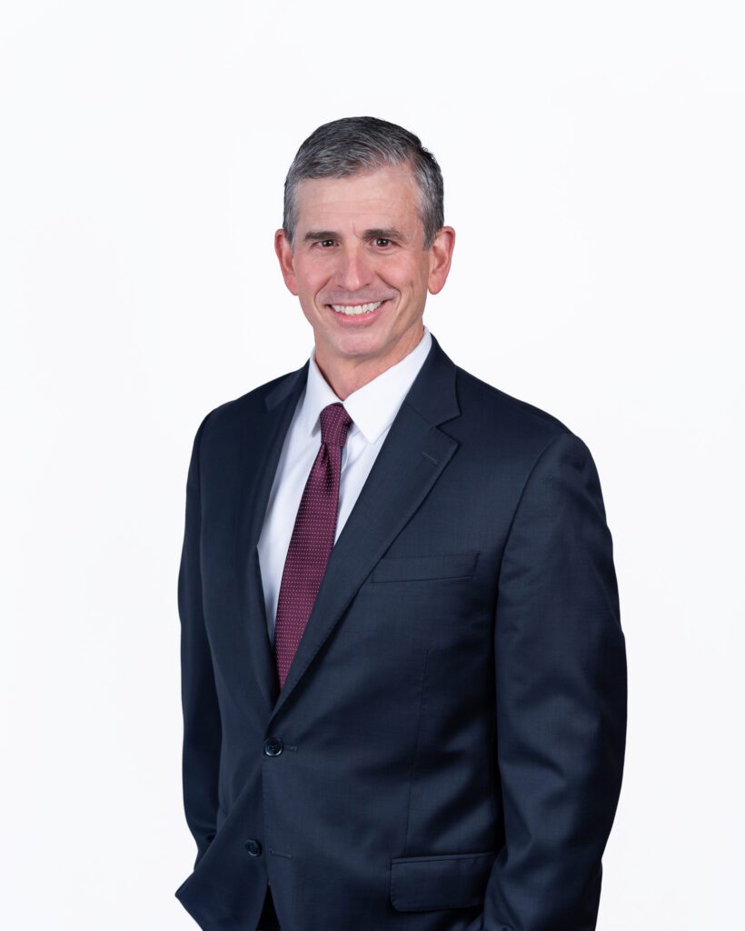 A male public speaker smiling for his headshot session with a white backdrop.