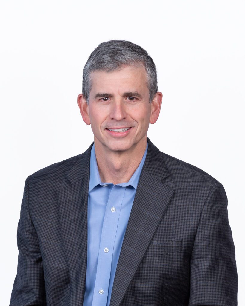 A male public speaker smiling for his headshot session with a white backdrop.