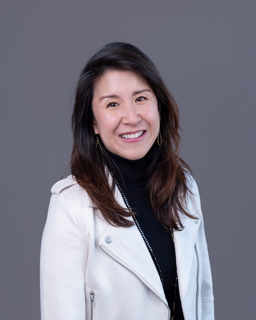 A female Asian executive coach & advisor smiling for her headshot session with a gray backdrop.