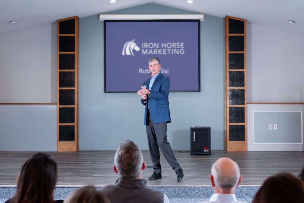A male public speaker talking on the stage with a live audience.