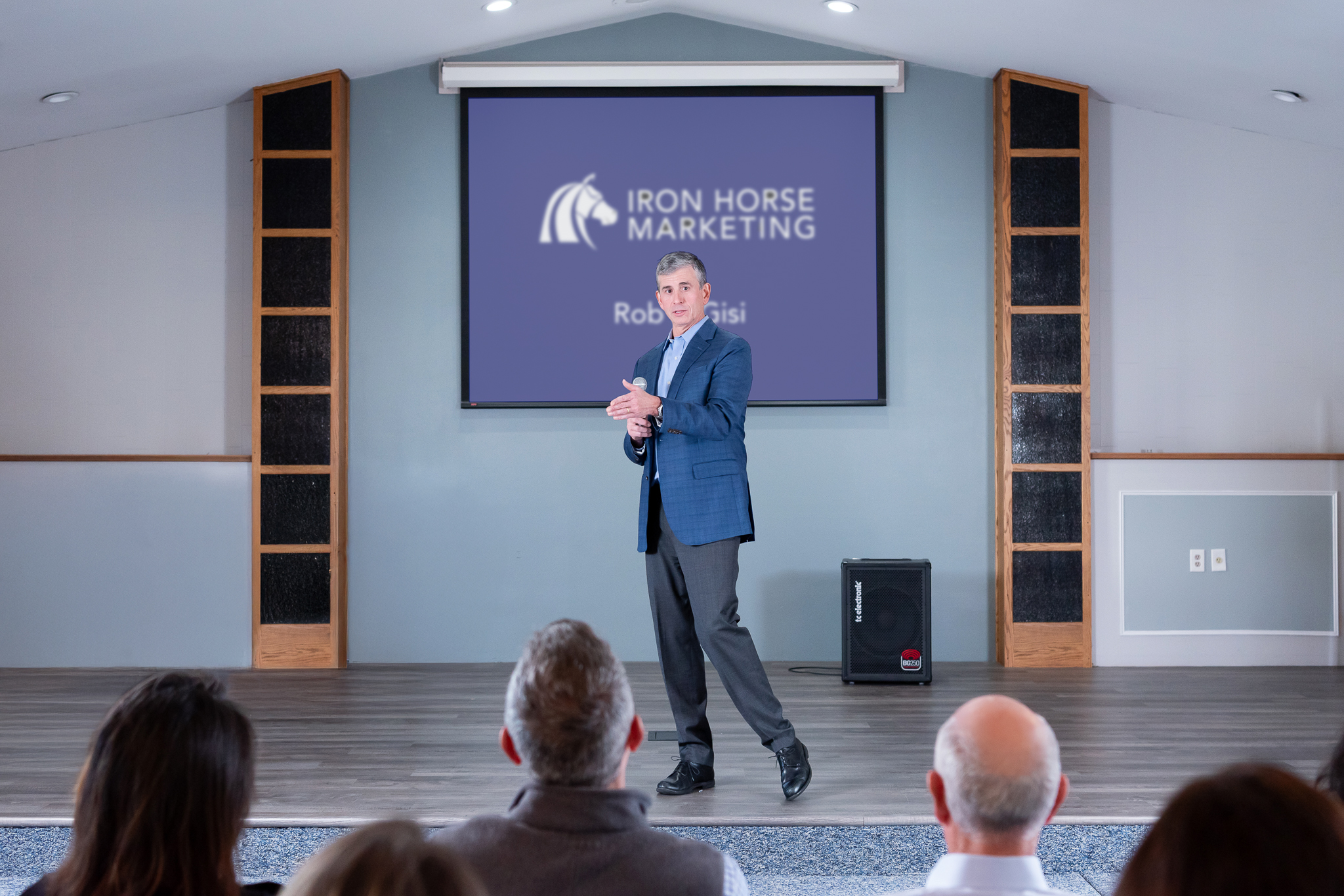 A male public speaker talking on the stage with a live audience.