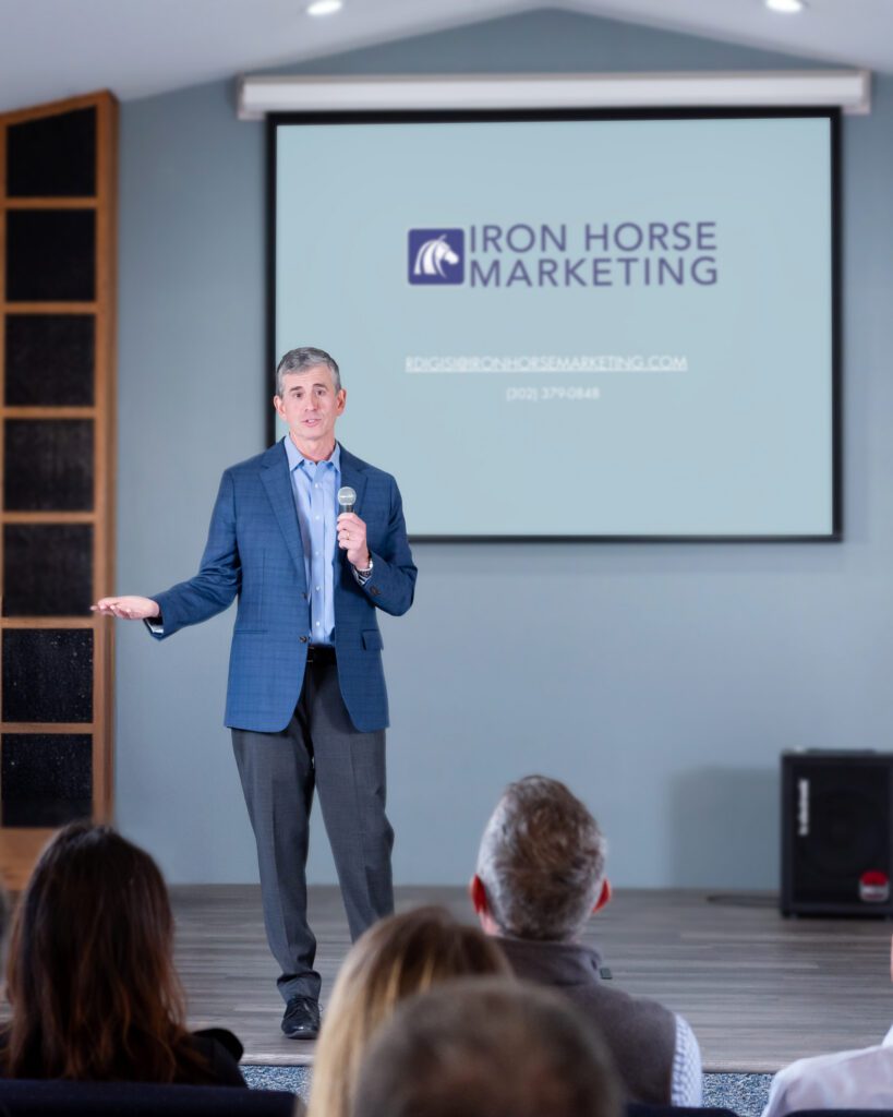 A male public speaker talking on the stage with a live audience.