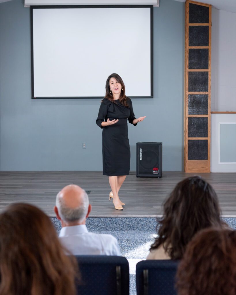 A female Asian executive coach & advisor speaking on the stage with a live audience.